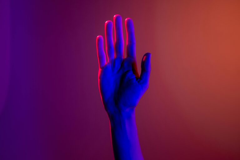 A single hand under neon lighting creating a colorful visual effect.